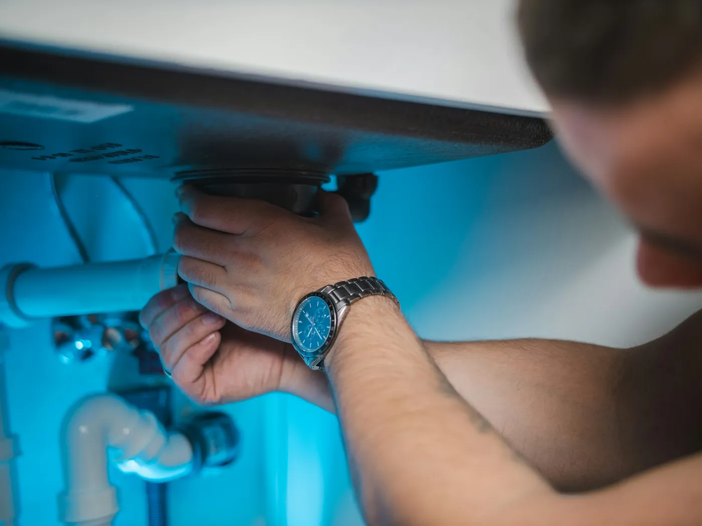 A tradesperson repairing plumbing under a sink