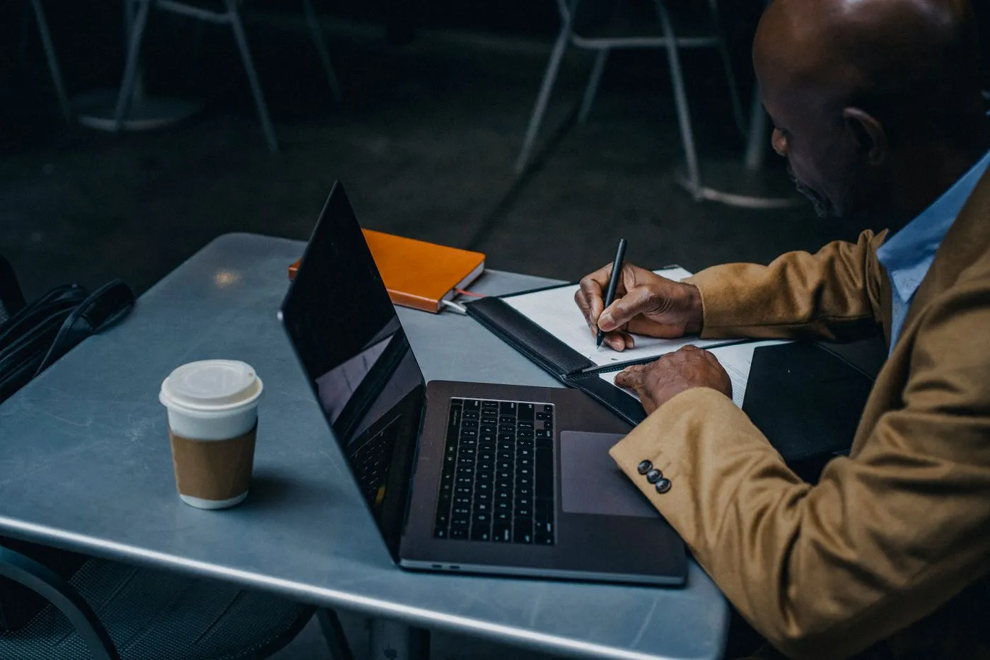 A business owner writing notes beside a laptop and coffee at a cafe table
