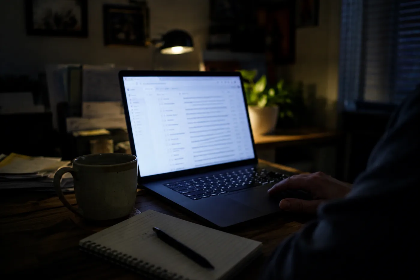 A laptop showing an email inbox in a dimly lit office at night