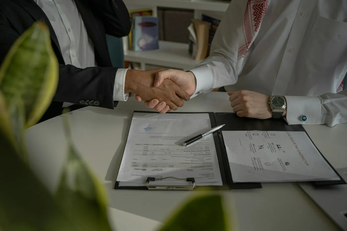 Two people shaking hands over a signed contract on a clipboard